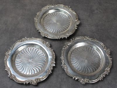 trois assiettes en argent ornées de motifs, posées sur une table
