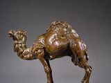 une statue en bronze représentant un chameau, posée sur un socle en bois