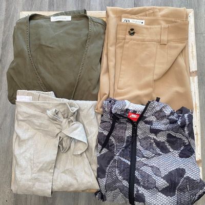 trois paires de pantalons pour homme dans une boîte posée sur un plancher en bois