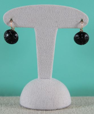 une paire de boucles d'oreilles noires et dorées posées sur un présentoir blanc