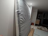 a person ' s hand pointing at a mattress in the corner of a room