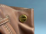 sac à main en cuir marron orné d'un bouton doré sur fond bleu