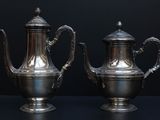 pair of antique silver teapots on a black background