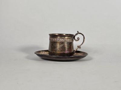une tasse et une soucoupe argentées posées sur une soucoupe, le tout sur une surface blanche