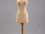 un mannequin en bois posé sur un socle en bois, devant un fond gris