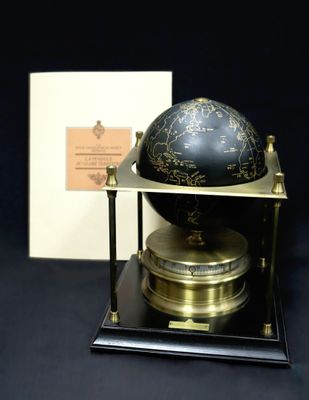 un globe noir et doré posé sur un socle, avec une boîte en arrière-plan