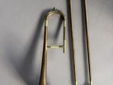 an image of a brass trombone and a trombone stick on a gray surface
