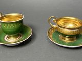 two green and gold cups and saucers on a gray surface