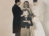 a black and white photo of a bride and groom feeding a cake to a young boy