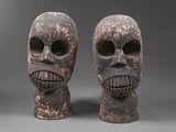deux masques en bois sculptés représentant des visages, sur fond gris