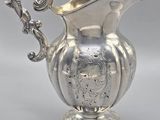 an antique silver pitcher with ornate design on a stand