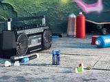 a boombox, a skateboard, a can of soda, and a can of water on the ground