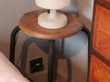a small table with a lamp on it next to a bed
