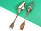 two silver spoons and a fork on a green and white surface