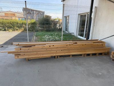 Plusieurs morceaux de bois sont empilés sur des palettes devant un bâtiment