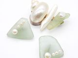 trois morceaux de verre de mer, accompagnés de perles et d'un coquillage, posés sur un fond blanc