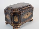 une boîte à bijoux ancienne, noire et dorée, posée sur une surface blanche