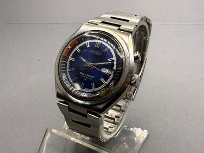 a silver watch with a blue face on a clear stand