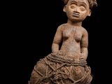 une statue représentant une femme assise sur un morceau de bois