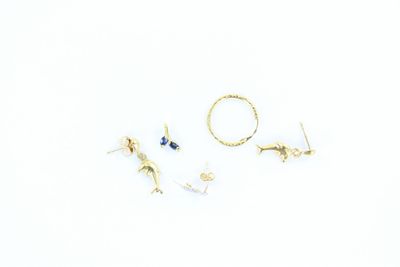 trois paires de boucles d'oreilles en or et une bague posées sur un fond blanc