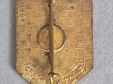 gold plated metal pin with a design on it on a white surface