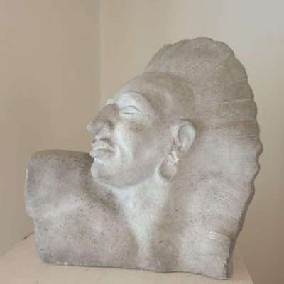 une sculpture en pierre représentant un homme coiffé d'une coiffe, posée sur une table