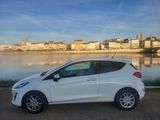 La petite voiture blanche est garée près de l'eau, devant la ville.