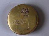 a small gold box with a purple flower on it