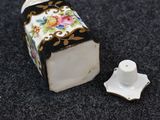 a small white box with a floral design on it next to a small white candle holder