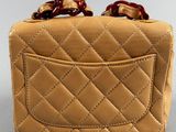 beige quilted purse with red handles on a white surface
