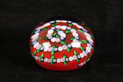 a red glass object with flowers on it on a black surface