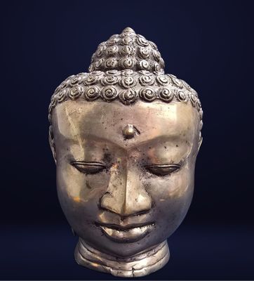une statue en argent représentant une tête de Bouddha sur fond noir
