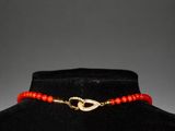 a red beaded necklace with a gold clasp on a mannequin neck