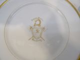 a white plate with a gold rim with a crest on it