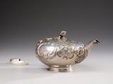 a silver teapot sitting on a table next to a ring