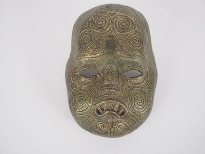 un gros plan d'un masque en bronze sur une surface blanche