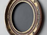 an oval mirror with a gold frame on a gray wall