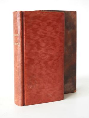 an old book sitting on top of a white table next to a red book