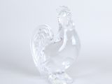 une figurine en verre transparent représentant un coq sur fond blanc