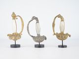 trois figurines en argent et en or posées sur des socles, sur une surface blanche
