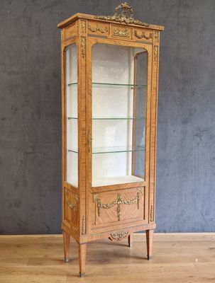 une vitrine en bois avec des étagères en verre, posée sur un parquet