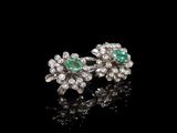 une paire de boucles d'oreilles en émeraude et diamant posées sur un fond noir