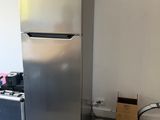 a silver refrigerator in the corner of a room next to a trash can