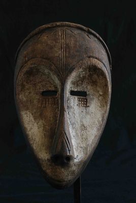 un vieux masque en bois posé sur un socle, sur fond noir