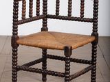 une photo représentant une chaise en bois avec une assise tressée, posée sur un parquet