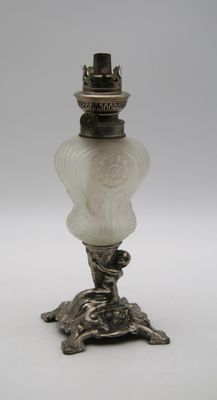 une lampe ancienne en argent et en verre dépoli, posée sur un pied en métal