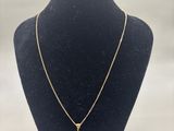 a gold necklace with a white diamond on a black mannequin