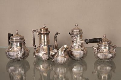 cinq théières en argent posées sur une table en verre