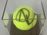 une balle de tennis jaune dans une boîte transparente sur laquelle figurent des inscriptions