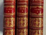trois livres rouges et dorés posés sur une surface blanche